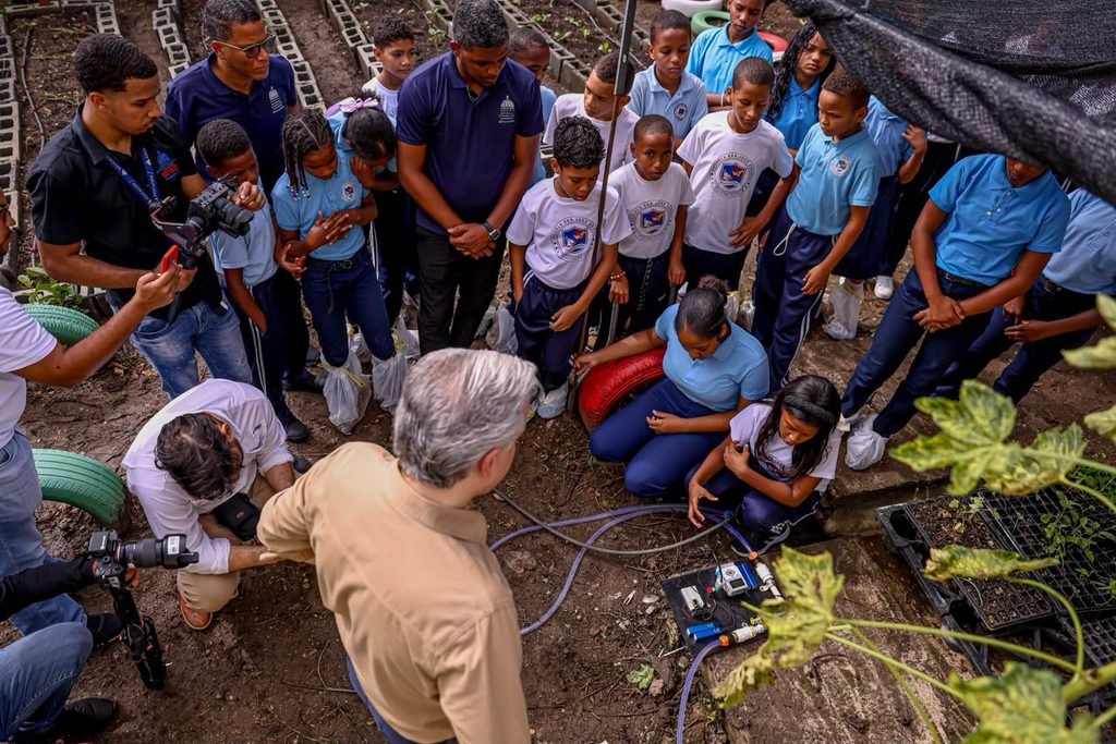 Estudiantes dominicanos desarrollan proyectos de robótica y riego automatizado para proteger el ambiente y resolver problemas reales, mientras que, De Camps observa el proyecto.